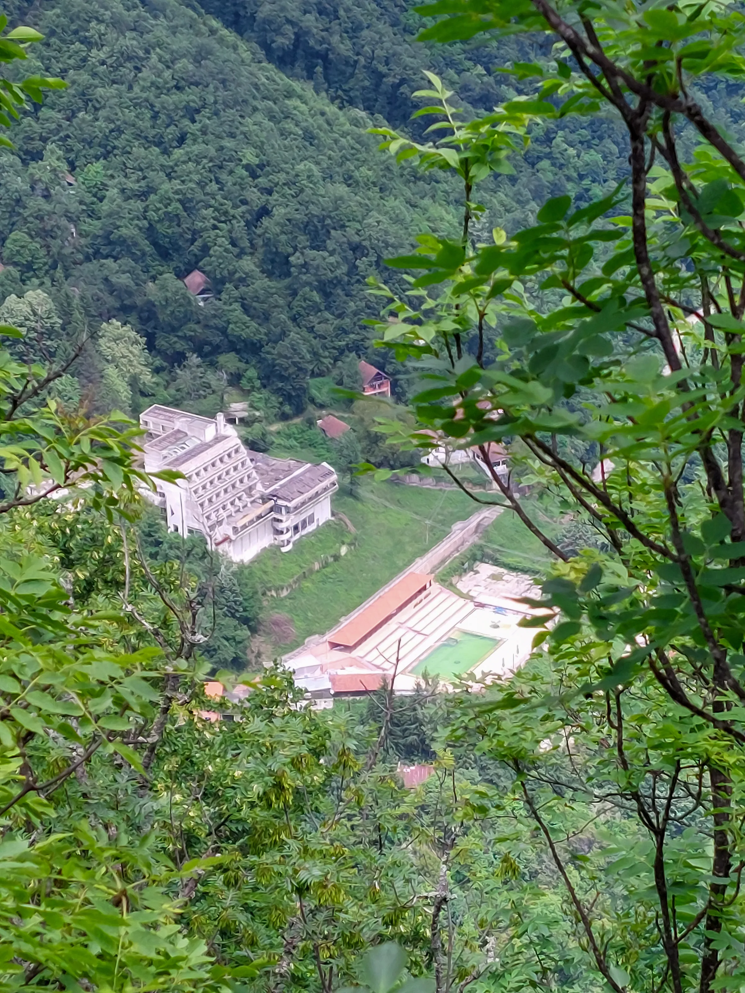 Hotel i bazeni Zvonačke Banje u šumovitoj dolini, snimljeni kroz lišće sa padine iznad